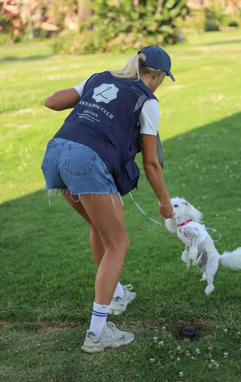 A small white dog jumping up at Alisa in a training session