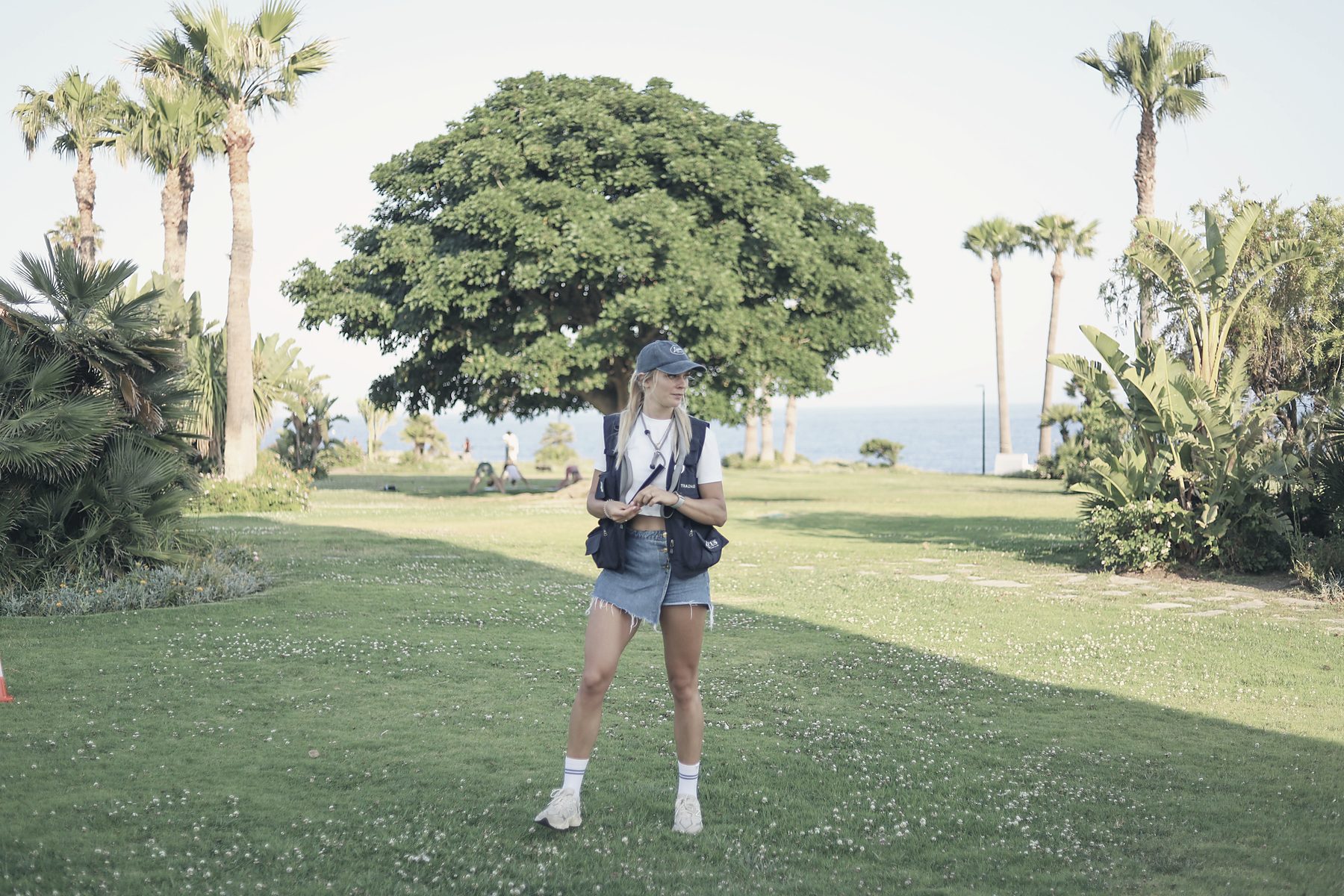 Alisa Groen alone on the seafront lawn under a broad tree, the sea beyond